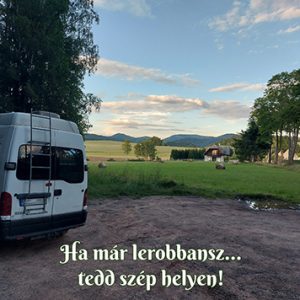 Lakóautó áll egy gyönyörű mezőn, hátérben hegyek, az ég szép kék.